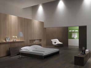 Schlafzimmerimpression mit Holzverkleidung an Wand Schlafzimmerimpression von Bett, Nachtisch und Sideboard mit Holzverkleidung an Wand und indirektert Beleuchtung